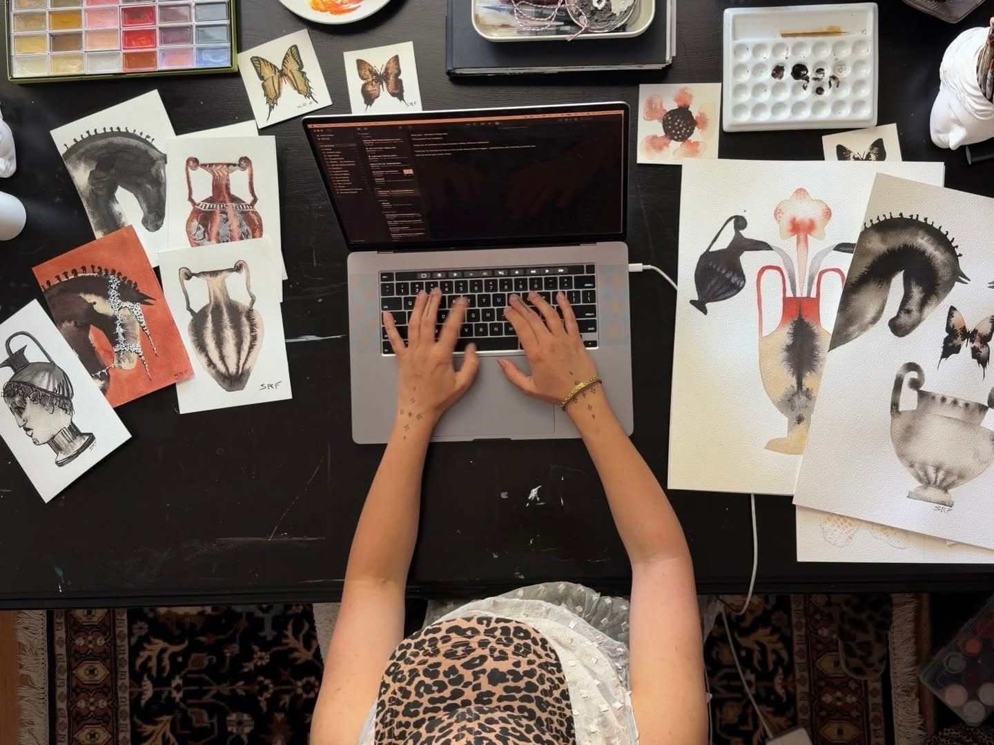 Desk laid out with paint palettes, illustrations and a laptop running an edit
